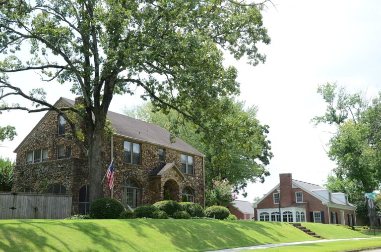 Stone two-story house under a large oak tree on a sloped lawn in the Hillcrest Historic District of Little Rock, Arkansas