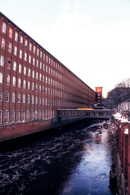 Brick mill building with footbridge over snowy river in New Hampshire, USA.