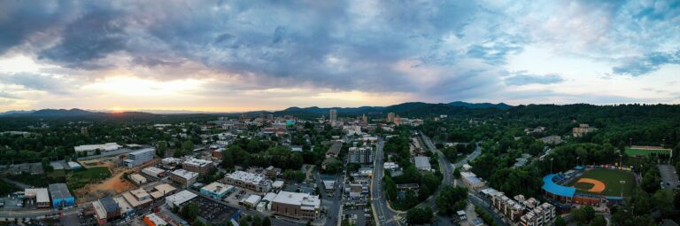 Aerial view of downtown Asheville, North Carolina at sunset, with McCormick Field in the foreground and the Blue Ridge Mountains behind